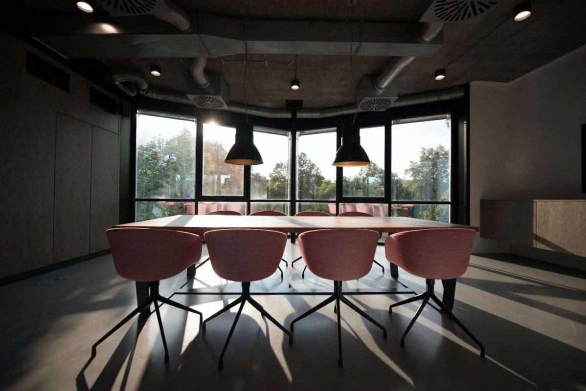 Möteslokal med 8 rosa kontorsstolar kring ett bord och vackert ljus från ett stort fönster.